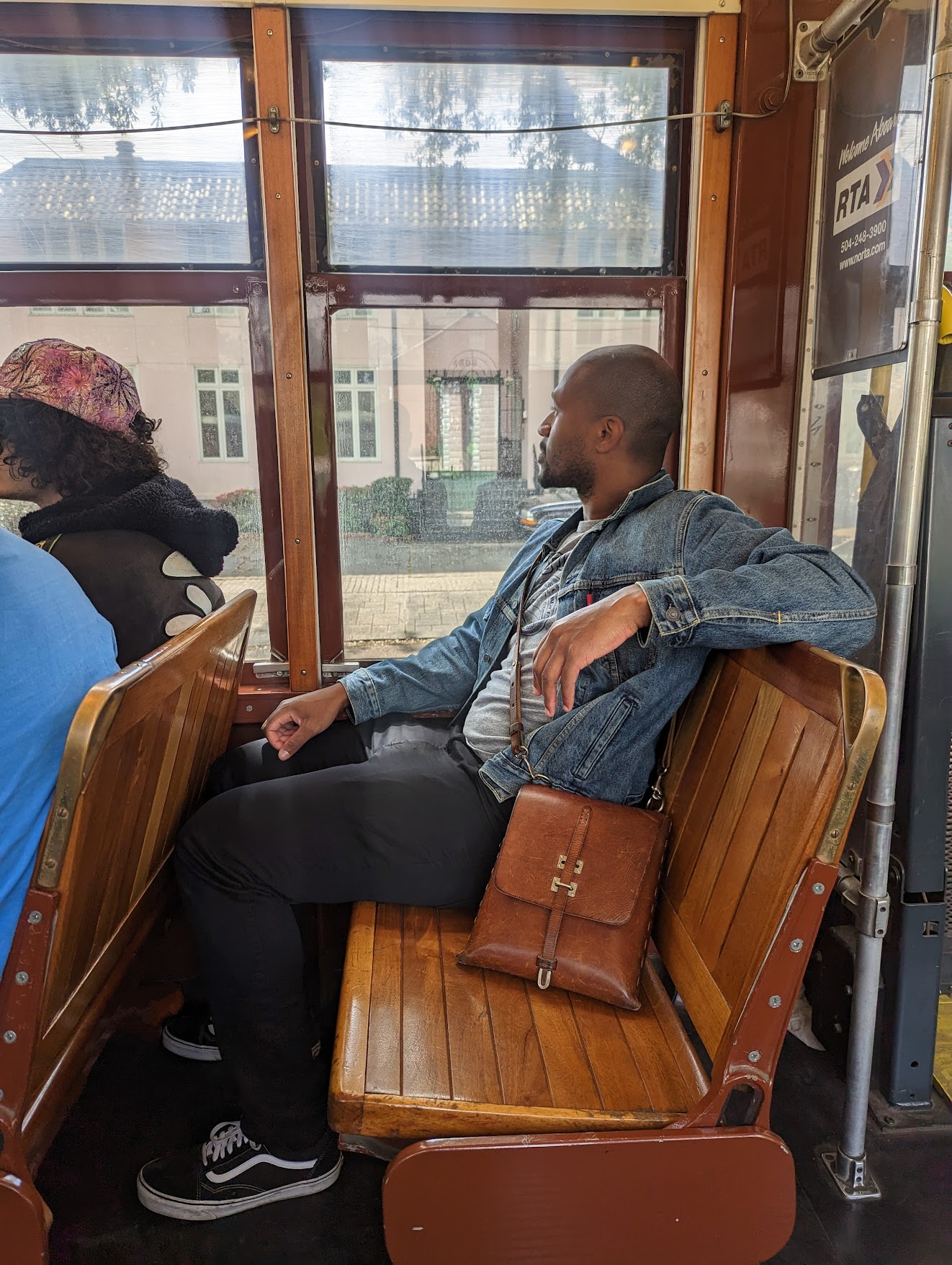 Me wearing a jean jacket sitting on a trolley with a leather satchel